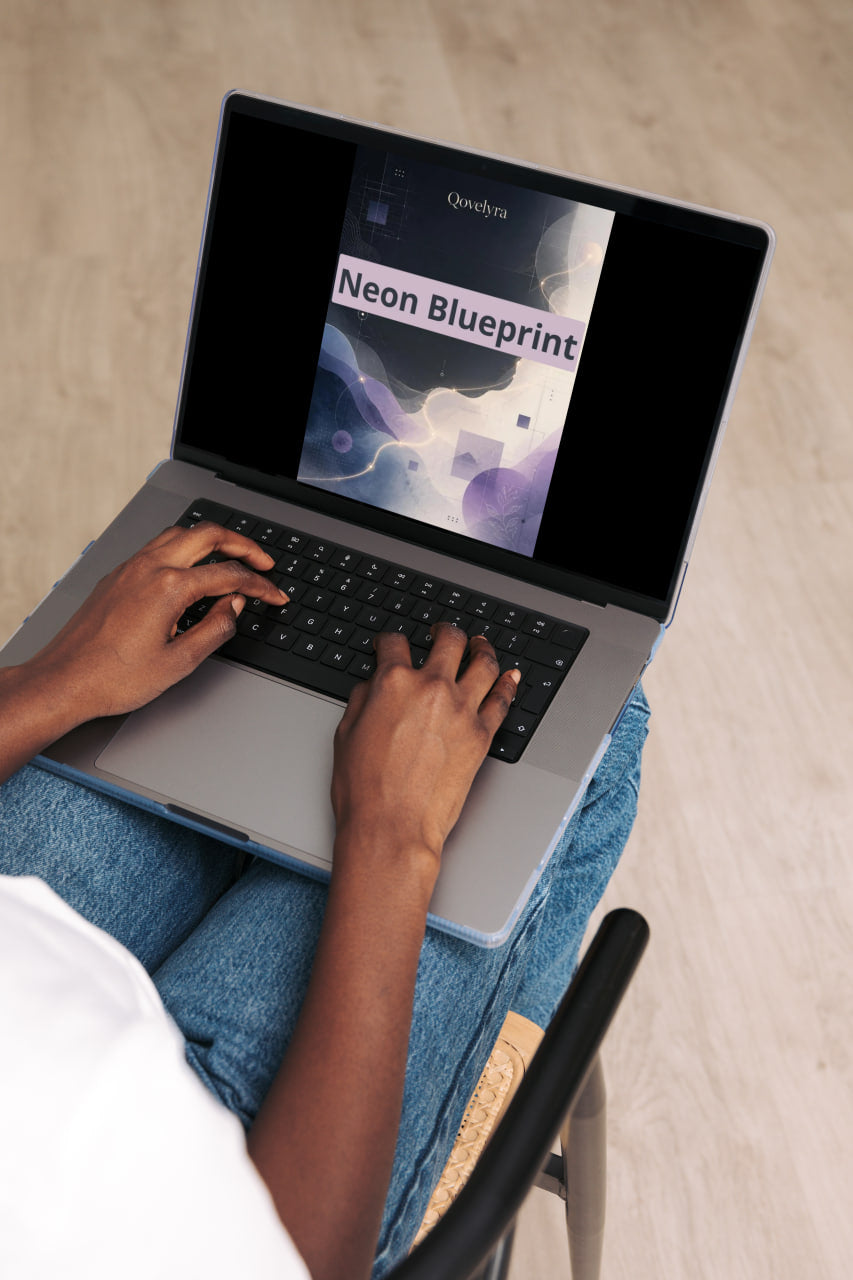A person typing on a silver laptop with blue jeans and a white shirt visible, with the laptop screen displaying a digital cover titled 'Neon Blueprint'.